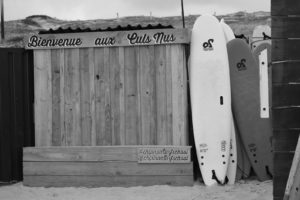 grayscale photo of surfboard on wooden fence